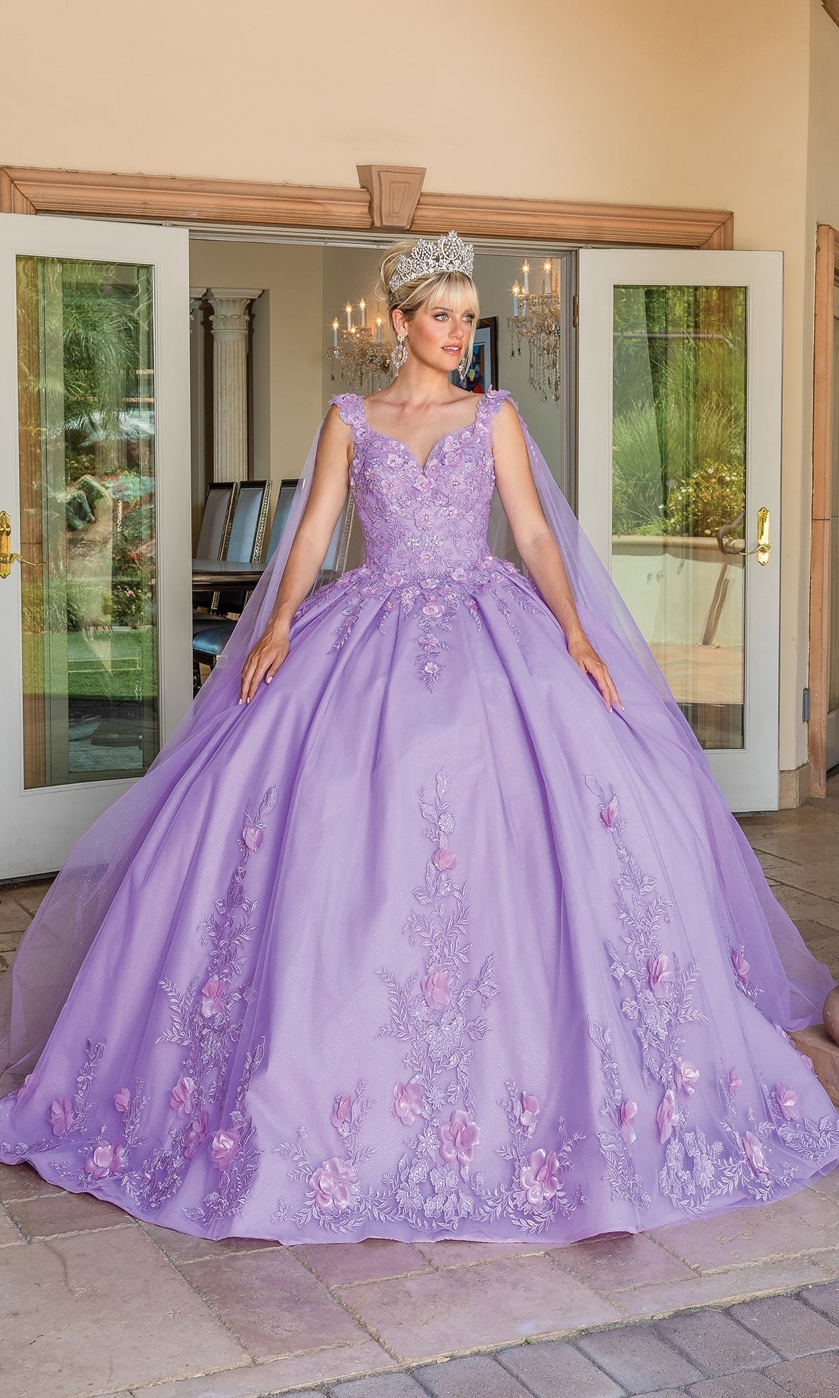 A woman stands in front of open double doors wearing the Quinceanera Dress 1716 By Dancing Queen, a sleeveless lilac ball gown with floral embroidery, a sweetheart neckline, and a sparkling tiara.